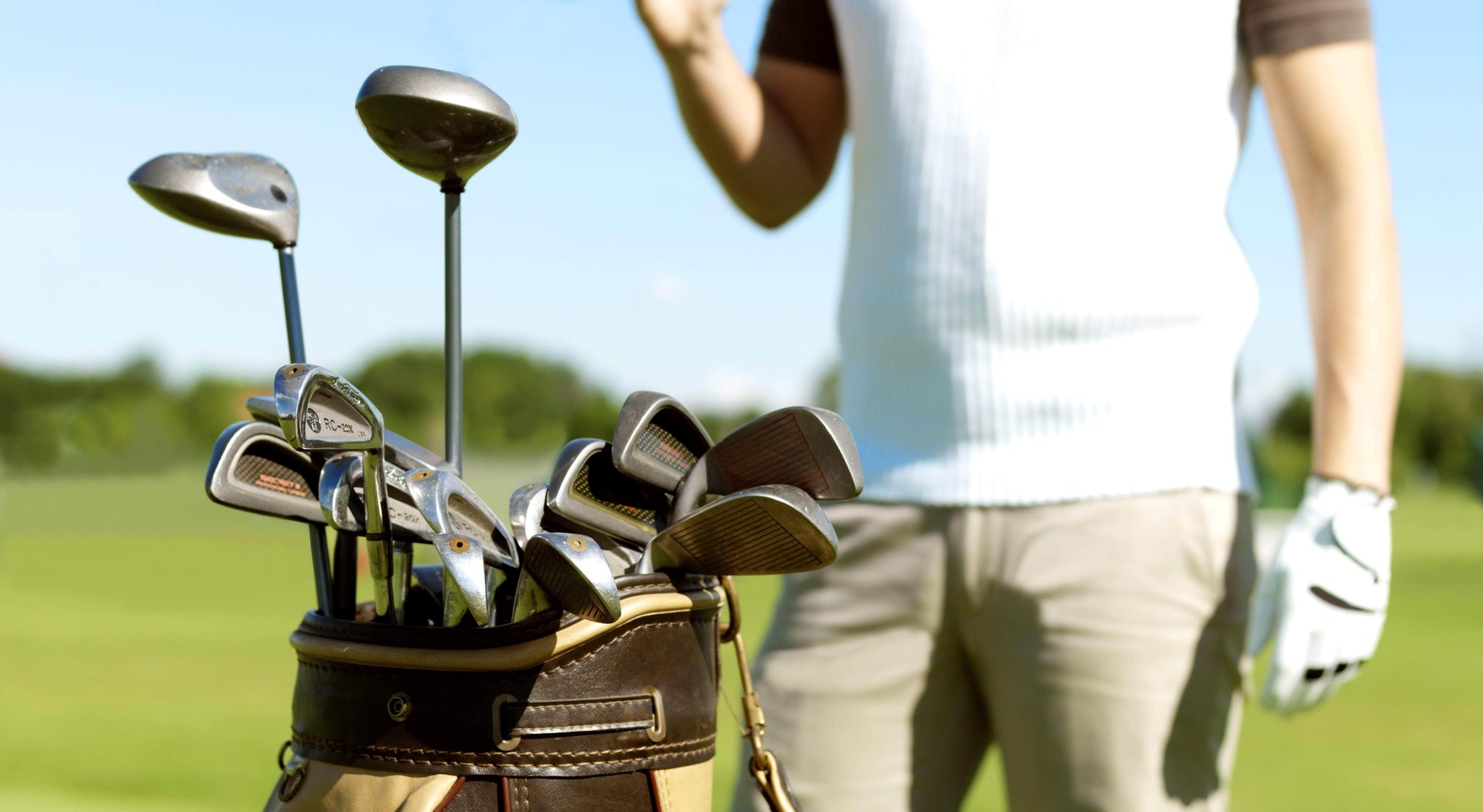 Premium golf uniforms and golf apparel for golf players and clubhouse staff. Male golfer on course with clubs in foreground